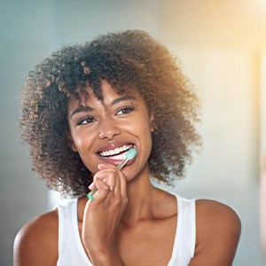 Woman in white tank top brushing teeth at bathroom mirror