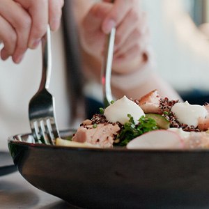 Hands scooping salad onto plate with forks