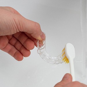 Patient using toothbrush to clean aligner