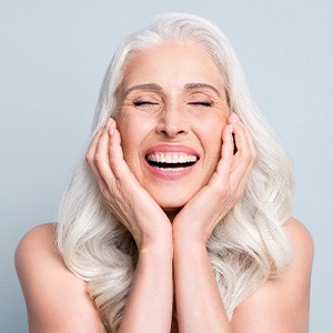 Woman with long white hair smiling with eyes closed framing face with hands