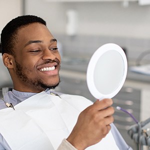 Man smiling at reflection in handheld mirror
