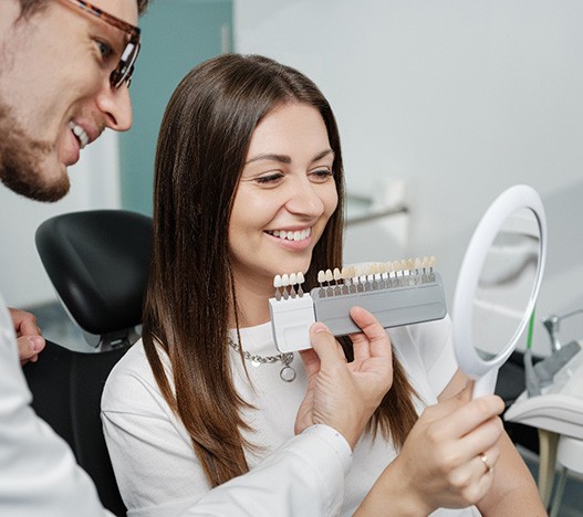 Woman smiling while looking at different shades of veneers