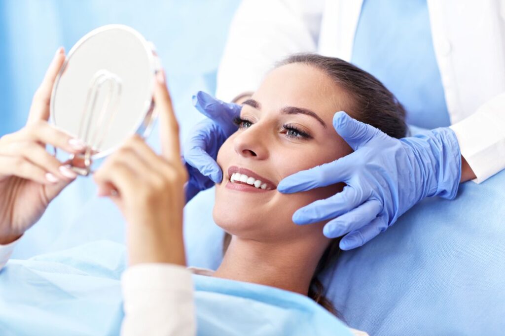 A woman in a dental chair looking at her newly improved smile in a mirror.
