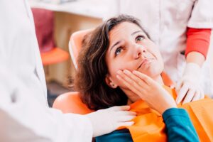 Worried-looking patient sitting in dentist’s chair holding mouth in pain.